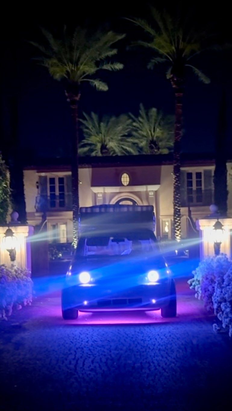A Capri Car glowing purple in front of a lit estate at night